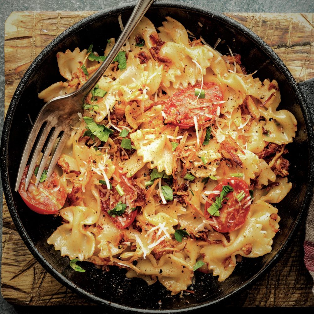pasta farfalle with roasted meat and tomatoes in a frying pan